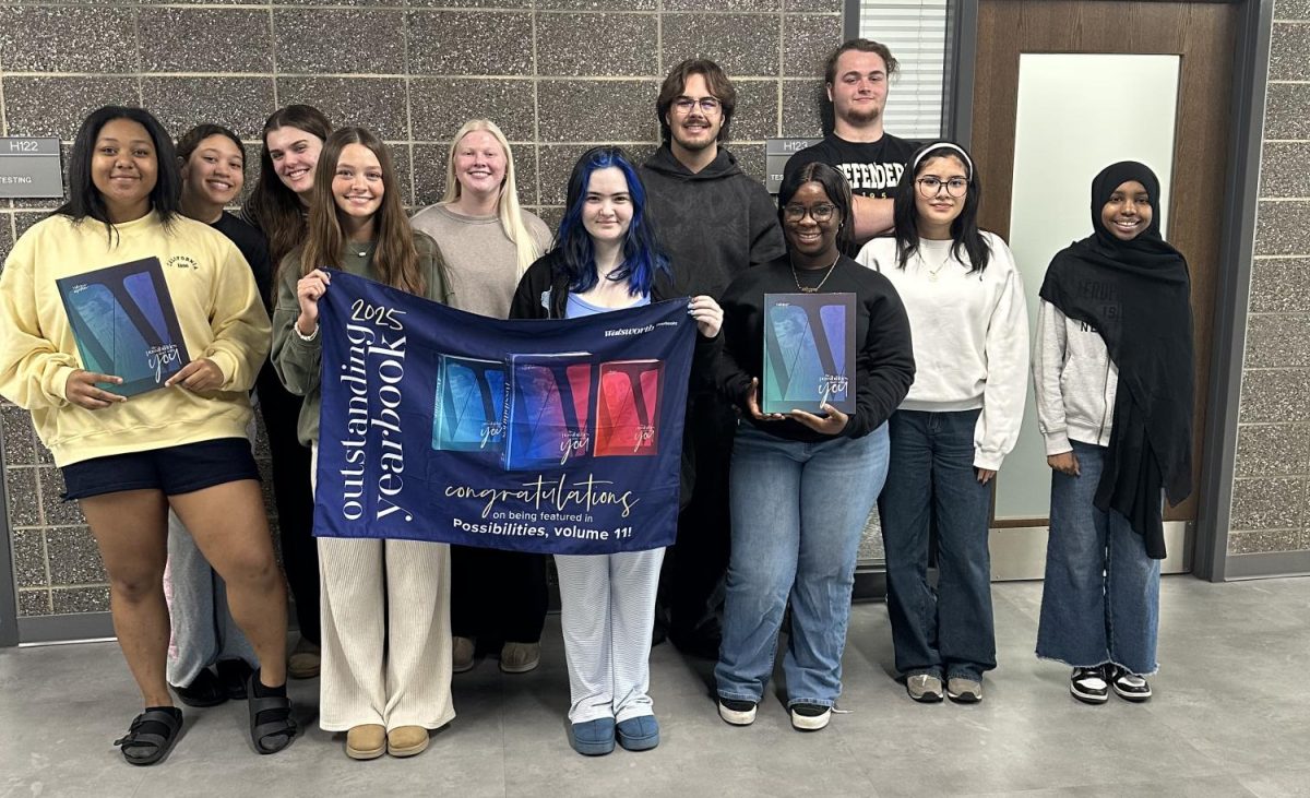 The 2026 yearbook staff poses with a banner celebrating the 2025 book being featured in the Walsworth Possibilities Book.